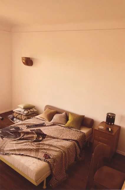 Bedroom interior featuring a made bed with a patterned blanket, pillows, a wooden nightstand, and a brown wooden chair. 