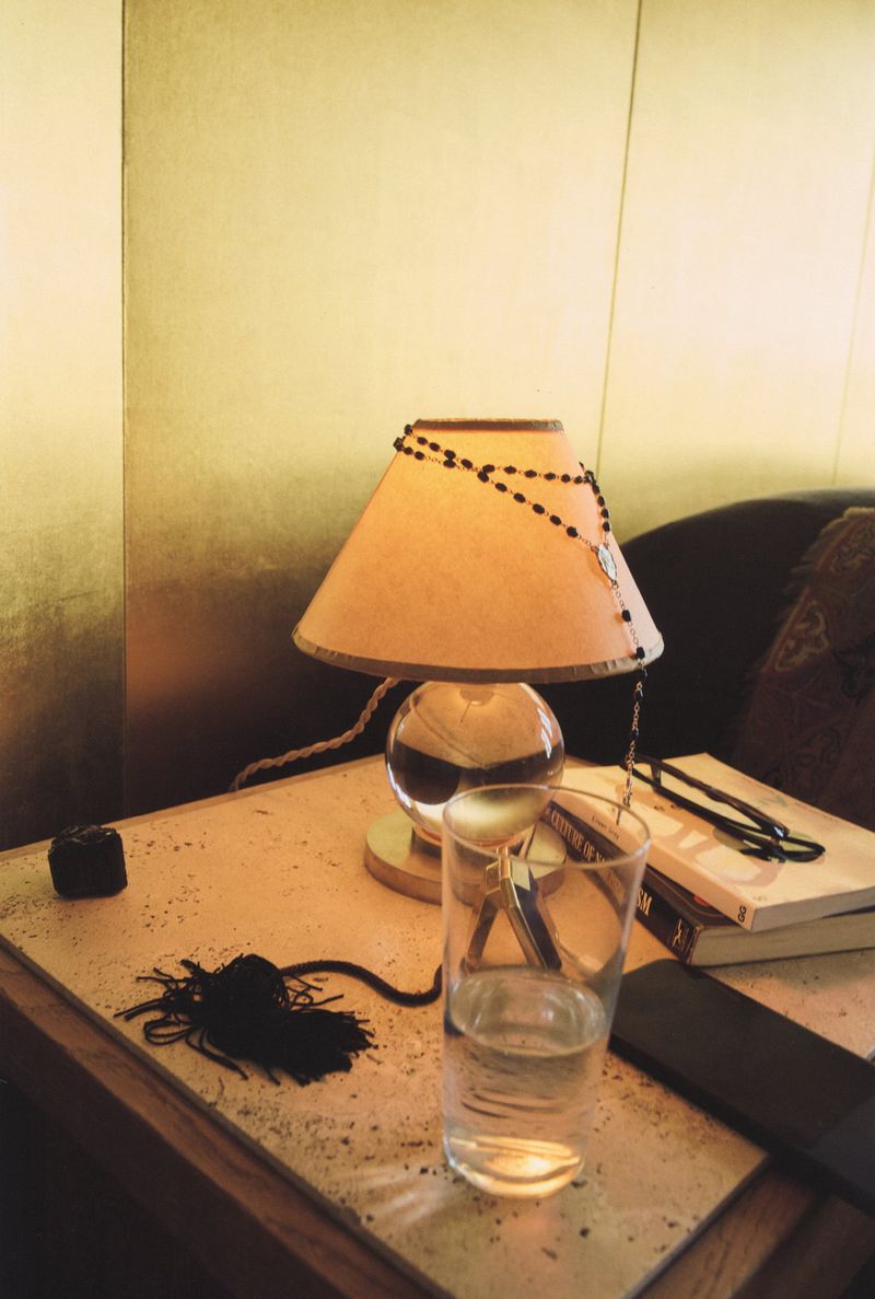 A nightstand setting with a glass of water, lamp, and books creates a cozy, warm ambiance with soft lighting and golden background.
