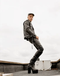 Model Ben Mickleburgh posing on an urban rooftop wearing a black leather jacket, fitted pants, and extreme platform boots.
