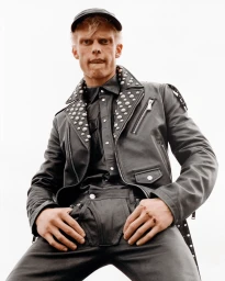 Model Ben Mickleburgh wearing a studded black leather jacket, cap, and leather pants in a low-angle shot against a white background.
