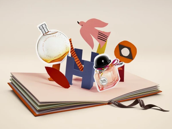 Two perfume bottles are showcased in a pop-up style book, complemented by abstract geometric shapes, paper bird, and a brown branded ribbon.