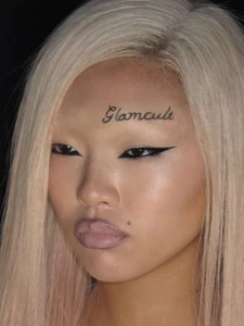 Close-up beauty portrait of an East Asian model with platinum hair, sharp winged eyeliner, and Glamcult scripted above the eyebrow.