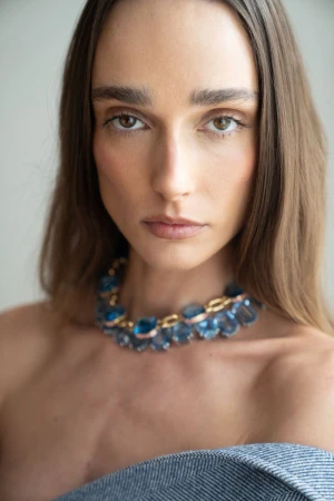 Close-up portrait of an adult woman with blue gemstone necklace, featuring soft lighting and a neutral background.