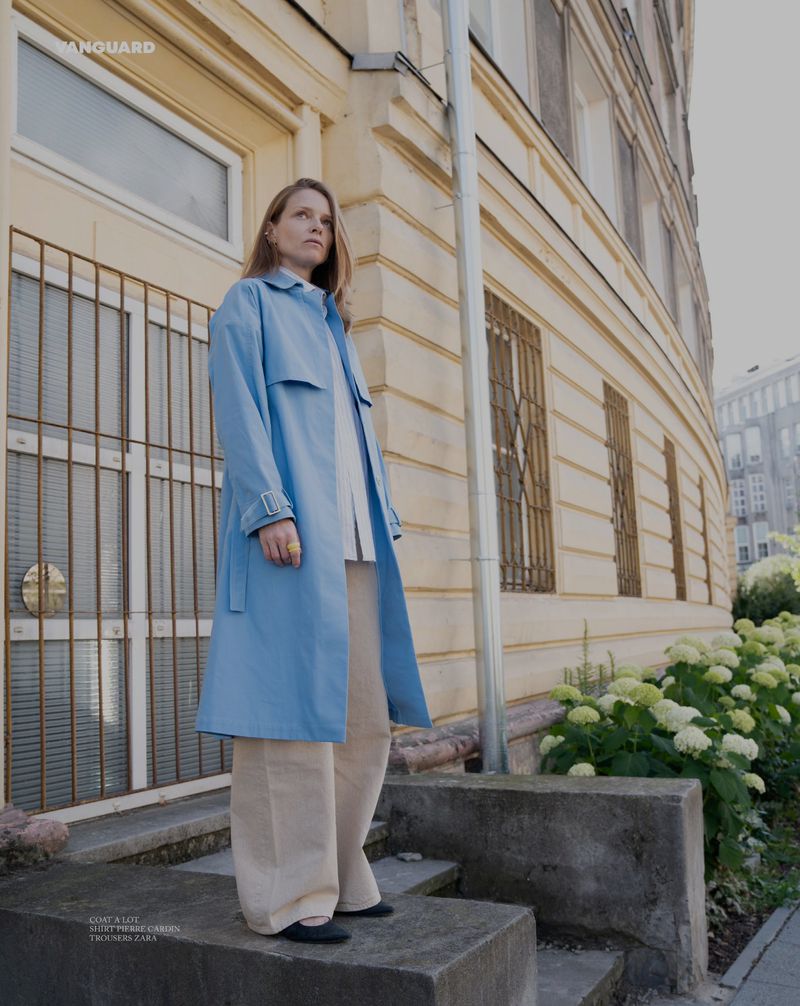 Woman in a blue coat stands on concrete steps in front of a building, posing in an urban setting with natural light.