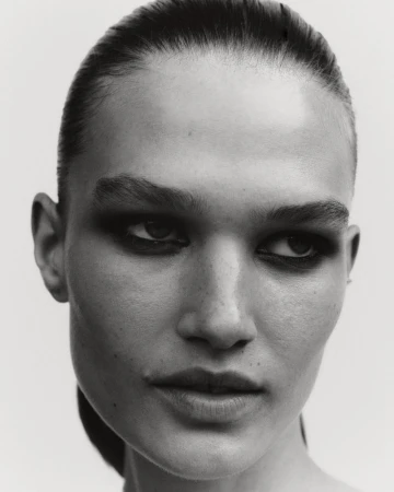 Monochrome portrait of a woman with slicked-back hair and dramatic eye makeup in a studio setting. High-contrast, beauty shot.