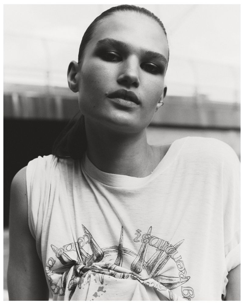 Monochromatic portrait of a young woman with slicked-back hair wearing a graphic tee shirt in an outdoor setting.