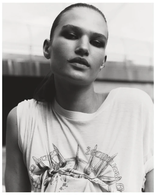 Monochromatic portrait of a young woman with slicked-back hair wearing a graphic tee shirt in an outdoor setting.