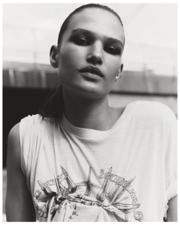 Monochromatic portrait of a young woman with slicked-back hair wearing a graphic tee shirt in an outdoor setting.