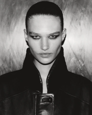 Monochrome portrait of a woman with sleek hair and dark makeup, wearing a black leather jacket against a textured background.