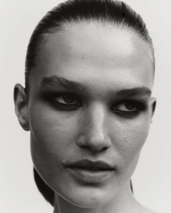 Black and white close-up portrait of model Emmi Freeman with dark smokey eye makeup and slicked-back hair.