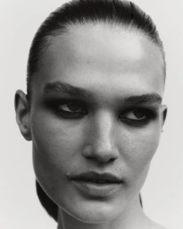 Black and white close-up portrait of model Emmi Freeman with dark smokey eye makeup and slicked-back hair.