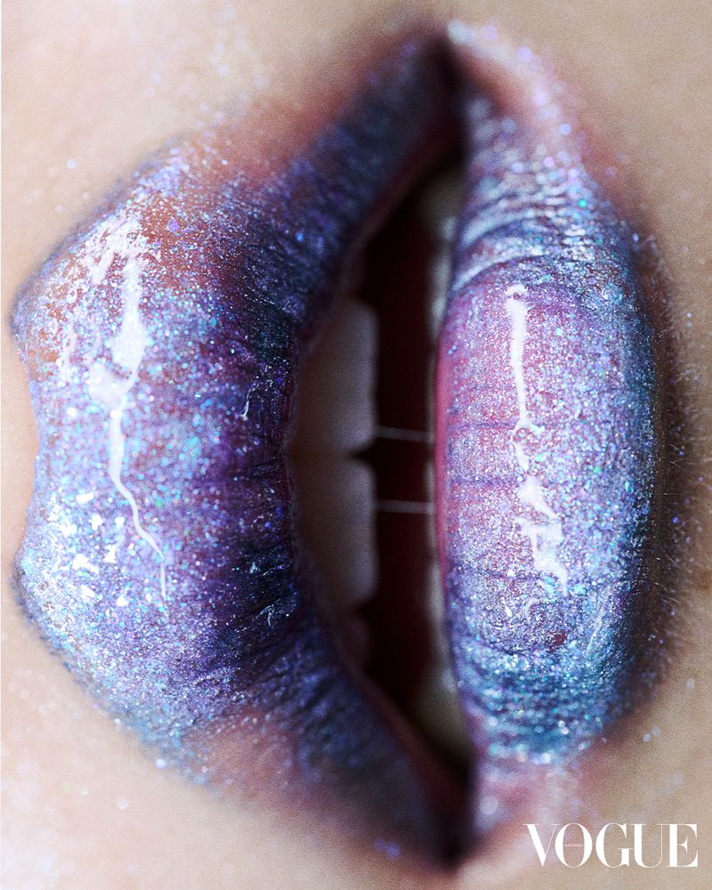 Macro shot of person's lips with shimmery, glossy purple lipstick and visible teeth, conveying high fashion and beauty concept.