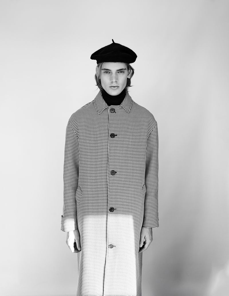 Portrait of a young adult male in a black beret and patterned coat, posing in a studio with soft, diffused lighting.