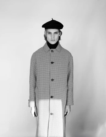 Monochrome portrait of a male model wearing a patterned button-down coat and a black beret against a seamless white studio backdrop