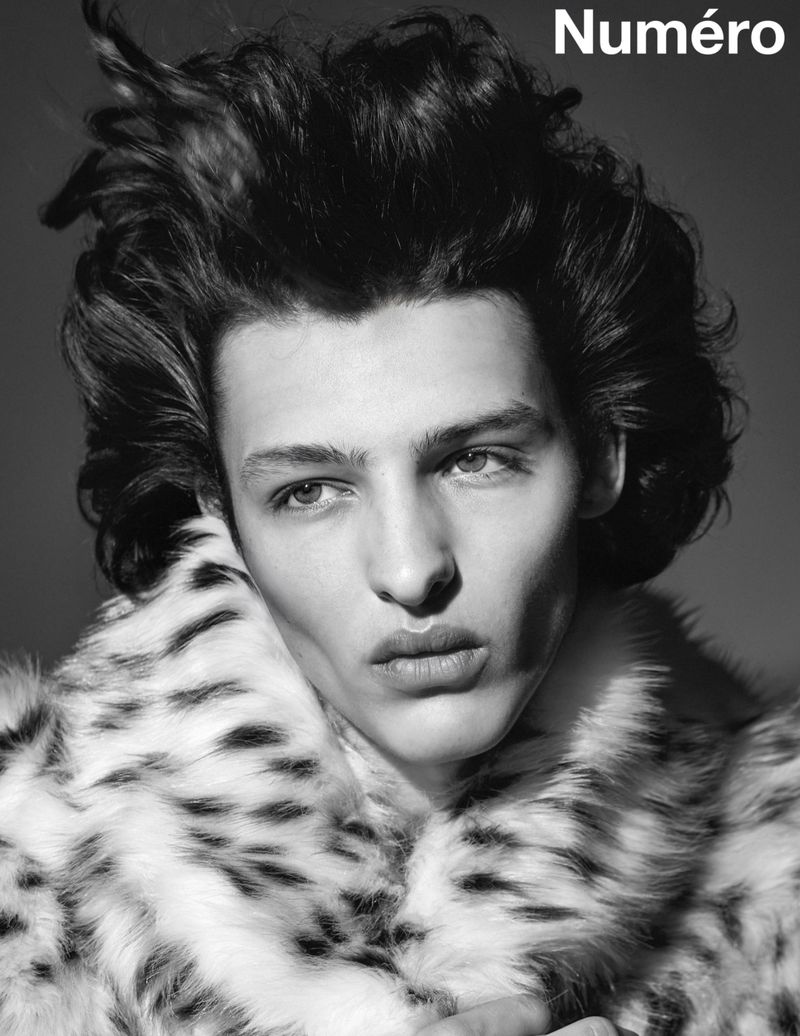 Black and white portrait of a male model with dark wavy hair wearing a fur coat in a studio setting with the text 'Numéro' visible.