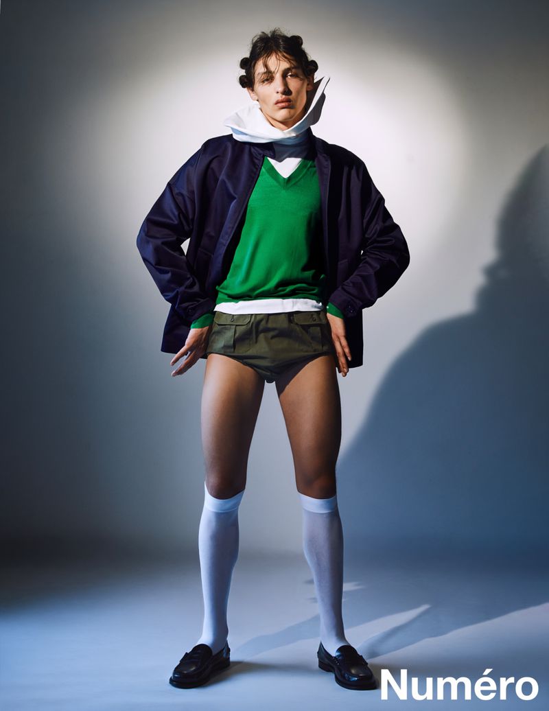Fashion editorial shot of a male model in retro-inspired clothing, posing in a studio with a spotlight effect and the logo "Numéro" visible.