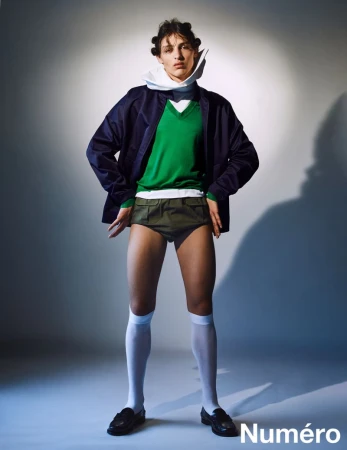 Fashion editorial shot of a male model in retro-inspired clothing, posing in a studio with a spotlight effect and the logo "Numéro" visible.