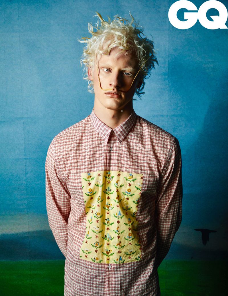 Albino male fashion model with unique facial features poses wearing a red and white patterned shirt in front of a blue background for GQ.