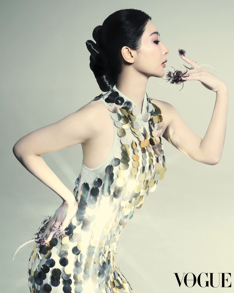 Elegant woman in a sparkling halter dress posing in a studio with theatrical spiders on her hand for a Vogue fashion shot.