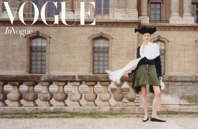 Fashion editorial showcasing a model in a historical-inspired outfit against a stone building with windows, promoting Vogue Hong Kong.