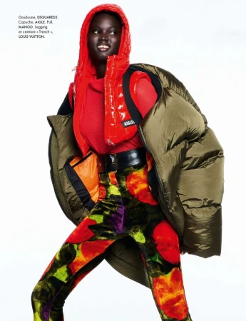 Fashion editorial shot of a Black female model in a red puffer vest, green coat, and patterned leggings against a white backdrop.
