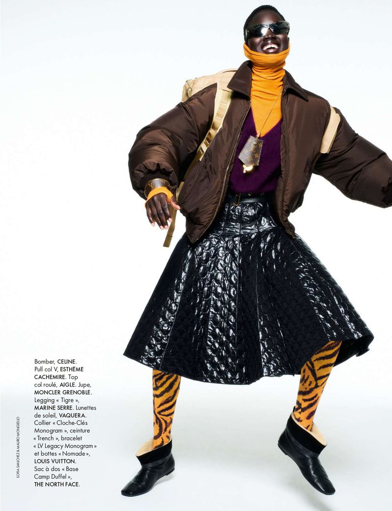 Woman in an oversized brown puffer jacket, purple top, and black quilted skirt poses against a white background with tiger-striped leggings.