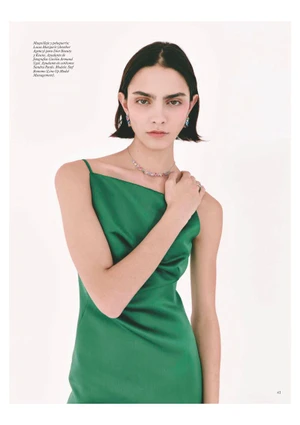 Model Stef Bonomo wearing an emerald green slip dress with delicate jewelry against a white studio background.