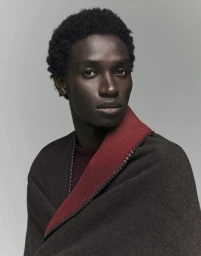 Model Modou Wade wears a dark brown woolen wrap with a red lapel against a neutral studio backdrop for Esquire Italia.