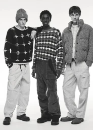 Three male models wearing patterned knit sweaters, winter trousers, and a beanie posing against a white studio background.