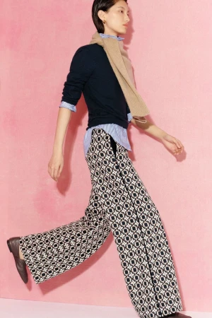 Model Xinyue Guo walks in wide-leg patterned trousers, a navy sweater, and beige scarf against a soft pink backdrop for ME+EM.