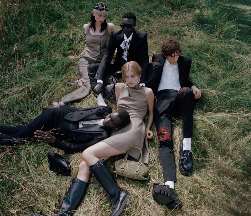 Five models lounging on a grassy field in tailored suiting and dresses for the Alexander McQueen Pre-collection.
