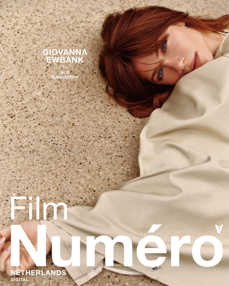 A young woman with auburn hair in a cream-colored coat rests on a speckled surface for a Numero Netherlands fashion editorial.