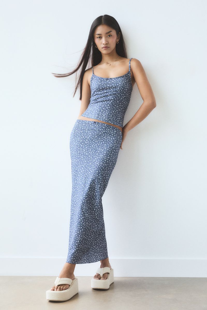 A young Asian woman poses in a blue floral-print spaghetti-strap dress and platform sandals against a white studio backdrop.