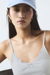 Model wearing a light blue cap and ribbed camisole top against a plain studio background.