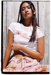 Model wearing a white floral t-shirt and pink patterned lounge pants against a wooden plank wall background.