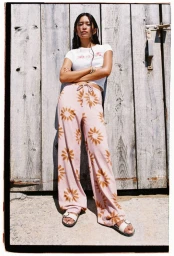 Model standing against vertical wooden planks wearing a white t-shirt and pink patterned trousers