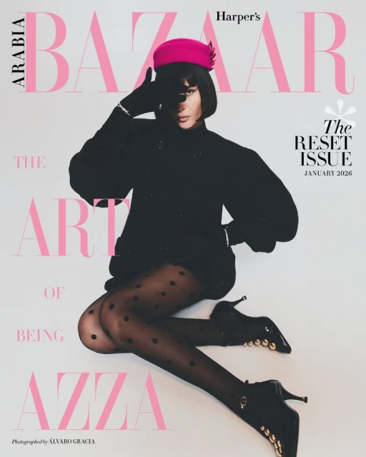 Azza Slimene posed in a black coat, polka dot tights, black heels, and a vibrant hot pink pillbox hat against a white background.