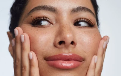 Close-up beauty portrait of a woman holding her hands to her face showcasing glossy lips and natural makeup