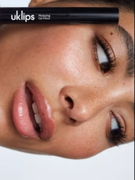 Extreme close-up beauty portrait of a person with glossy lips holding a black UKLIPS plumping lip gloss tube across their forehead