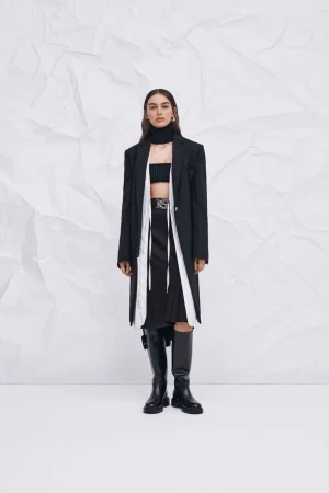 Fashion shot of an adult female wearing a black blazer, skirt and knee-high boots, posing against a white creased background.