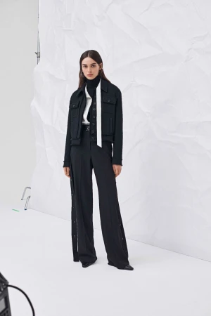 Studio shot of a woman in a black jacket and wide-leg pants against a white backdrop, modelling fashion, and wearing a turtleneck sweater.