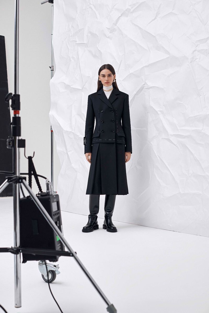 Fashion shoot featuring a woman in a black double-breasted blazer and skirt, posing in front of a white backdrop, and studio lighting.
