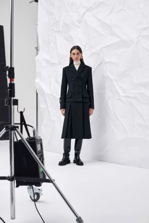 Fashion shoot featuring a woman in a black double-breasted blazer and skirt, posing in front of a white backdrop, and studio lighting.