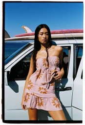 Model standing outdoors in front of a white vehicle carrying a surfboard, wearing a matching patterned strapless top and skirt.