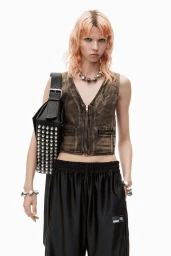 Model with dyed hair wearing a distressed vest and carrying a studded black handbag against a white background