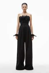 Model wearing a black strapless feather top and wide-leg trousers against a seamless white background