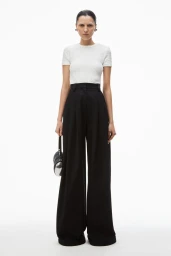 Model wearing a white t-shirt and wide black trousers holding a small black handbag against a white background