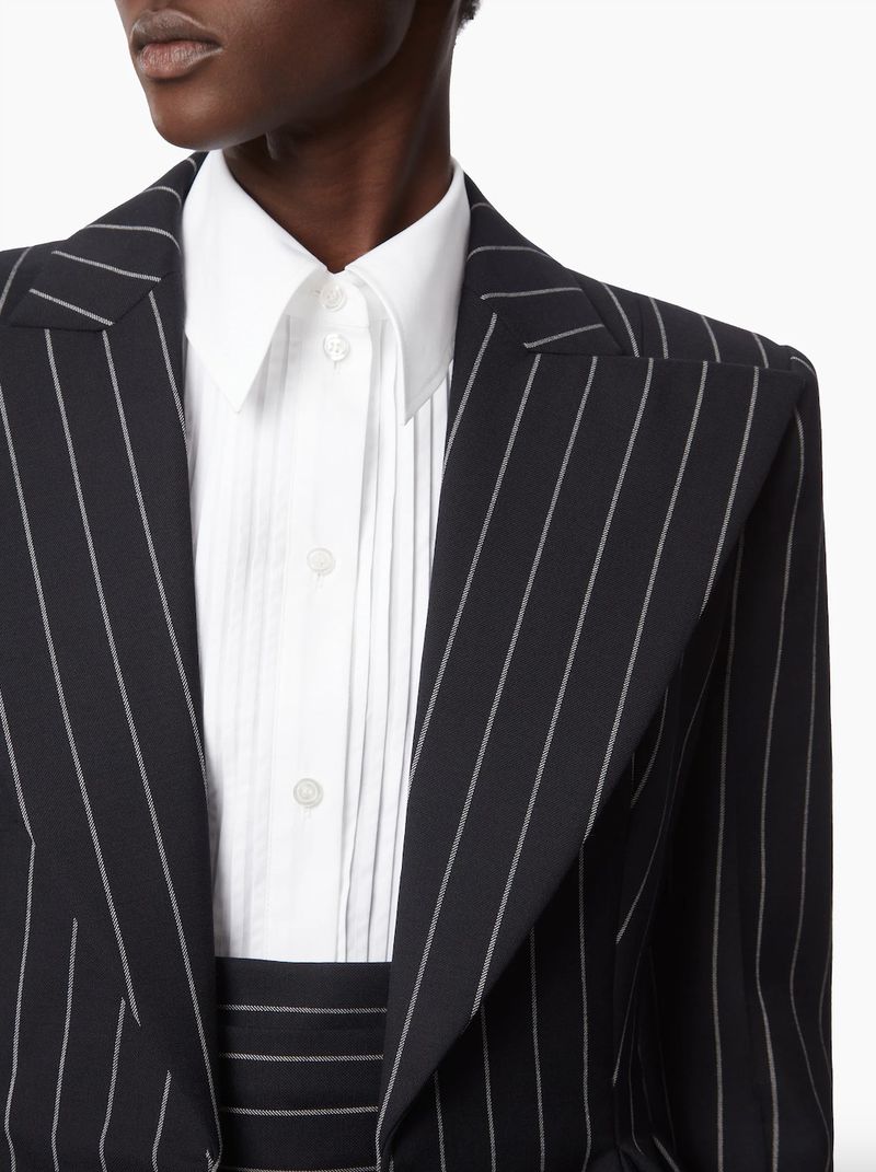 Close-up on a Black woman wearing a black and white pinstripe blazer with a white button-down shirt, showcasing fashion and style.