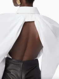 Model wearing a structured white open-back shirt and dark skirt against a plain white background for Nina Ricci FW24