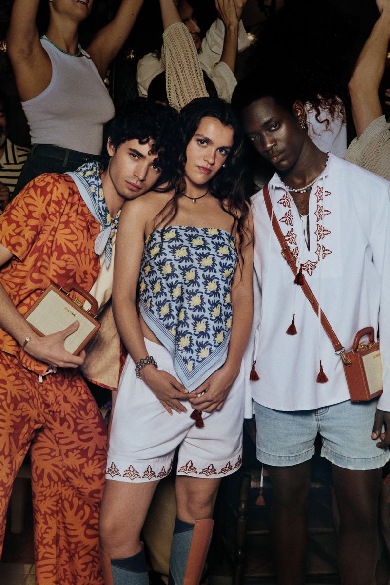 Three fashionably dressed individuals posing indoors, showcasing patterned shirts, shorts, and accessories against a blurred background.